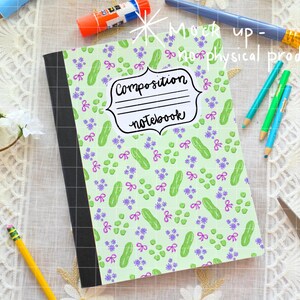 May include: Composition notebook with a light green cover featuring a pattern of green pickles, purple flowers, and pink bows. The notebook has a black spine and the words "Composition notebook" in a decorative frame.