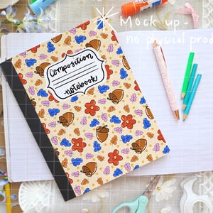 May include: Composition notebook with a beige cover featuring a pattern of acorns, flowers, and leaves in various colors. The notebook has a black spine and the words "Composition notebook" in a white label. Pencils and a pen are also visible.