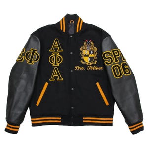 May include: Black varsity jacket with yellow and black detailing. It has black leather sleeves, yellow embroidered letters and patches, and the text "SP 06" on the right sleeve. The jacket has a button-up front and striped collar and cuffs.