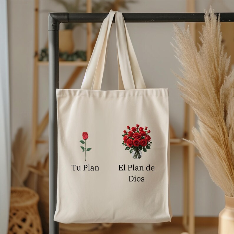 May include: A cream-coloured tote bag with two floral illustrations and text. One side shows a single red rose, the other a bouquet of red roses. Text reads "Tu Plan" and "El Plan de Dios".