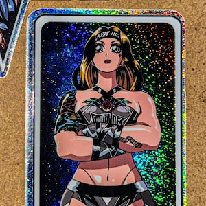 May include: A trading card featuring a stylized illustration of a muscular woman with blonde hair and a black and silver outfit. The card has a holographic border and the text "PAY NIG" on a headband. The card also has the text "SLANDER" at the bottom.