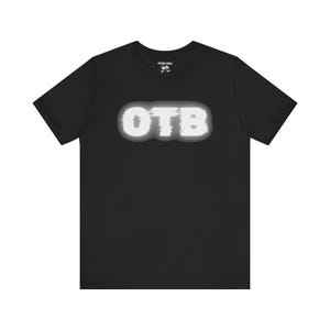 May include: Black t-shirt with a white "OTB" graphic printed on the front. The graphic has a glitch effect.