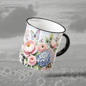 May include: White ceramic mug with a black handle and rim, decorated with a floral design. The design includes pink peonies, blue hydrangeas, a butterfly, and a birdhouse against a light blue gingham background.