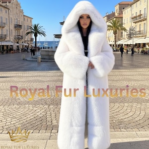 May include: A long, white fur coat with a large hood. The coat is floor-length and has a plush, textured appearance. The words "Royal Fur Luxuries" are displayed in gold lettering at the bottom of the image.
