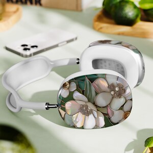 May include: White headphones with a floral design on one earcup. The design features white flowers with green leaves and iridescent accents.