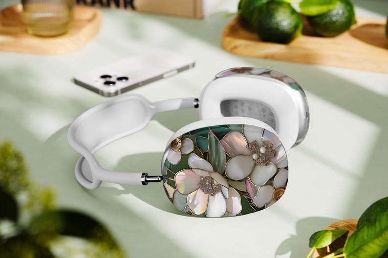 May include: White headphones with a floral design on one earcup. The design features white flowers with green leaves and iridescent accents.
