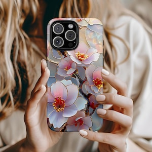 May include: A phone case with a floral design featuring delicate white and pink flowers with gold accents. The case has a clear back and a black camera cutout.