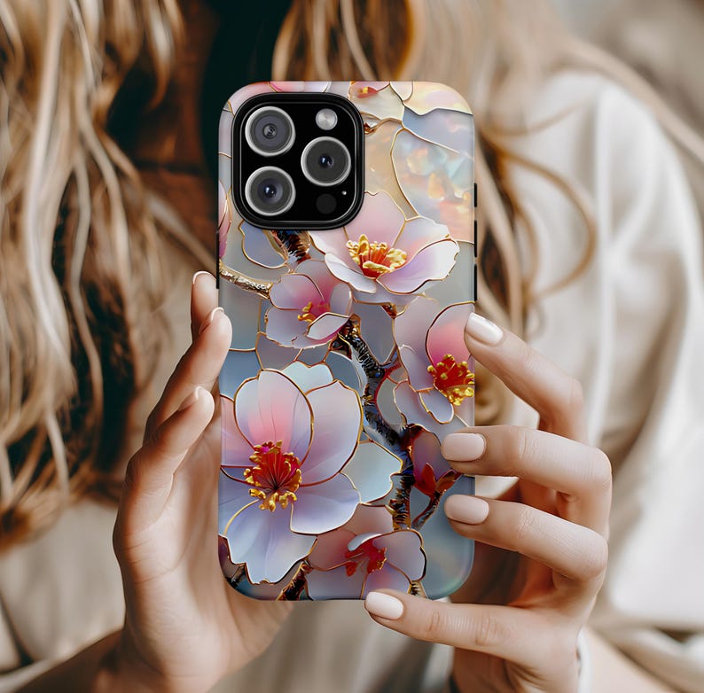 May include: A phone case with a floral design featuring delicate white and pink flowers with gold accents. The case has a clear back and a black camera cutout.