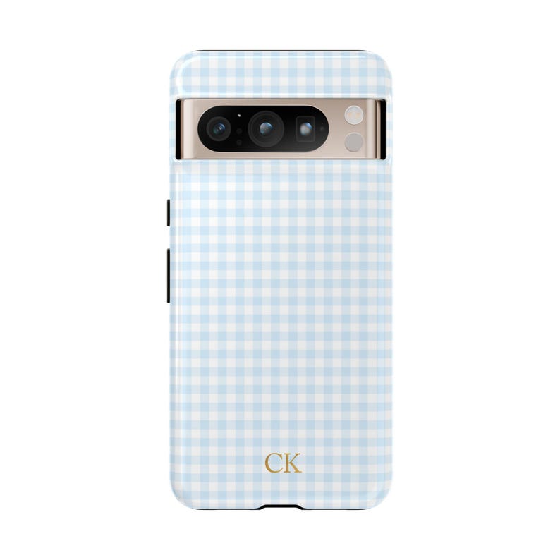 May include: A light blue and white gingham patterned phone case. The case has a camera cutout and the initials "CK" in gold at the bottom. The phone case is designed to fit a specific phone model.