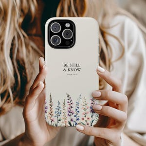 Op de afbeelding: Witte iPhone-hoes met een bloemenpatroon en de tekst "Be Still & Know Psalm 46:10".