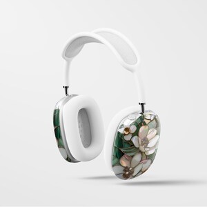 May include: White headphones with a floral design on one earcup. The design features green leaves, white flowers, and gold accents.