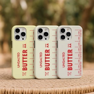 May include: Three phone cases in shades of yellow, cream, and white, each featuring the word "UNSALTED BUTTER" in red, with a measurement guide. The cases also display "NET WT. 4 OZ. (113g)" and "GRADE AA".