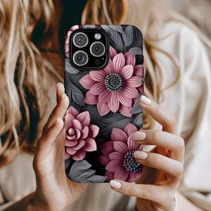May include: A phone case featuring a floral design with pink flowers and gray leaves on a black background. The case has a raised, three-dimensional effect, and the camera lenses are visible at the top.