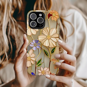 Op de afbeelding: Een telefoonhoesje met een bloemmotief in glas-in-loodstijl. Het heeft crème, paarse en oranje bloemen met gouden contouren en groene bladeren. De achtergrond is lichtbeige en de hoes heeft een glanzende afwerking.