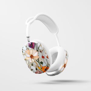 May include: White wireless headphones with a floral design on the earcups. The design features a variety of flowers in shades of pink, orange, yellow, and purple.