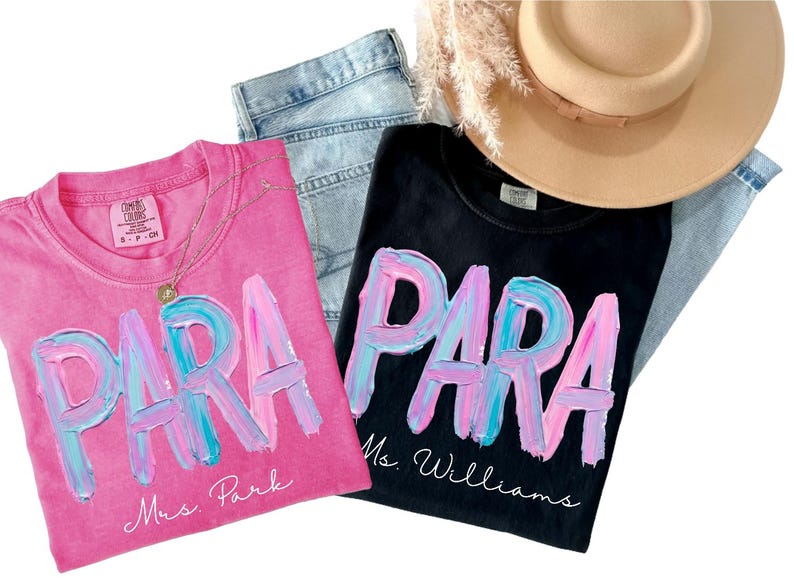 May include: Two t-shirts, one pink and one black, with the word "PARA" in a colorful, brushstroke design. The pink shirt says "Mrs. Park" and the black shirt says "Ms. Williams". A gold necklace, jeans, and a tan hat are also in the image.