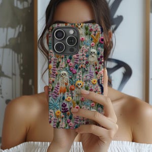 May include: A phone case featuring a colorful floral design with small skeleton figures. The case has a variety of flowers in shades of pink, purple, yellow, and orange. The skeletons are white and add a unique touch to the design.