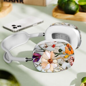 May include: White headphones with a floral design on the earcups. The design features a variety of flowers, including pink, purple, and orange, on a white background.