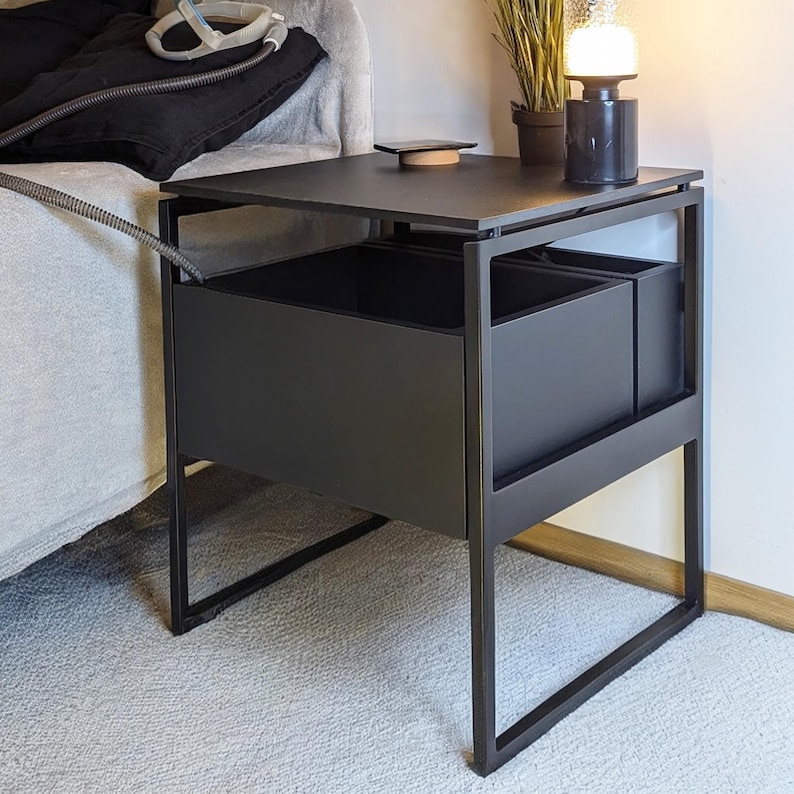 Puede incluir: Mesa auxiliar de metal negro con dos compartimentos de almacenamiento. La mesa tiene una tapa negra y un dise&ntilde;o simple y moderno.