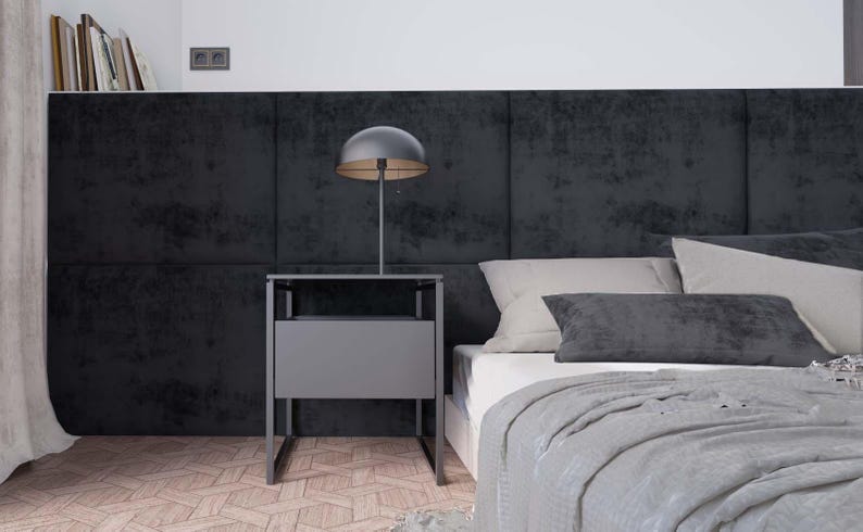 Puede incluir: Una mesita de noche negra con un caj&oacute;n y una l&aacute;mpara con una pantalla negra se encuentra junto a una cama con una cabecera gris y una manta gris.