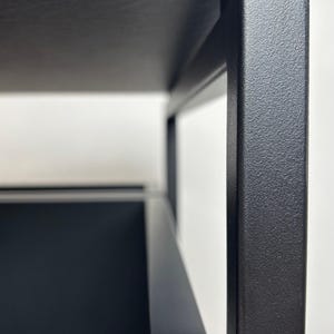 Puede incluir: Marco de metal negro con una tapa de madera negra y un caj&oacute;n negro. El marco est&aacute; hecho de metal grueso y tiene un acabado texturizado.