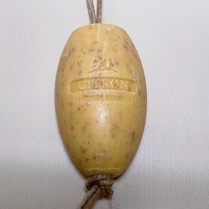Może przedstawiać: Żółte mydło z przywiązaną brązową sznurówką. Mydło ma nadrukowane słowa "Savon Citron" i "Fabriqué à Marseille".