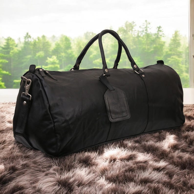 Puede incluir: Una bolsa de viaje de cuero negro con asa superior y una etiqueta de equipaje desmontable. La bolsa est&aacute; sobre una alfombra peluda de color marr&oacute;n.