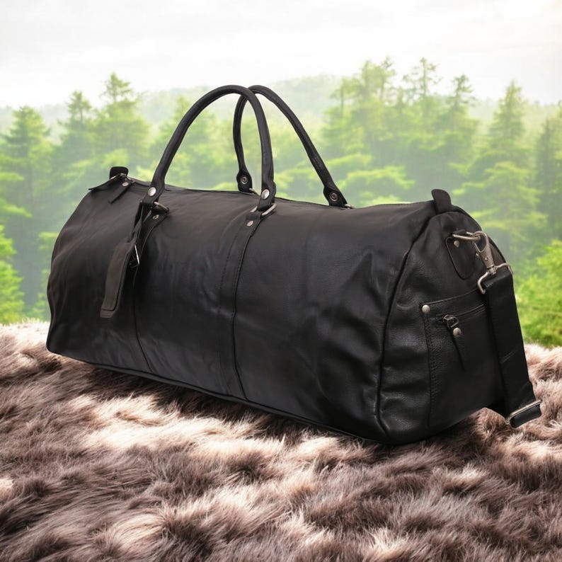 Puede incluir: Una bolsa de viaje de cuero negro con asa superior y bandolera. La bolsa tiene un bolsillo con cremallera en el lateral.