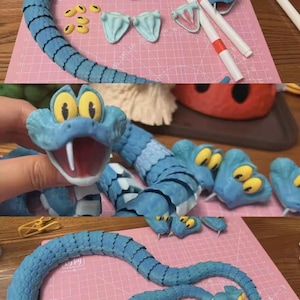 May include: A light blue snake sculpture with black markings, yellow eyes, and a white mouth. The sculpture is in various stages of assembly, with separate pieces including heads, tongues, and body segments. The background is a pink cutting mat.