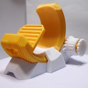 May include: A yellow and white 3D printed phone holder with a rotating base. The holder has a ribbed design and a curved shape to hold a phone securely.
