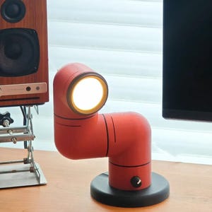 May include: A red articulated desk lamp with a black base and a white light bulb. The lamp is on a wooden desk.