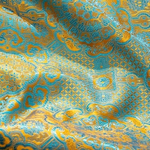 May include: Close-up of a patterned fabric with a repeating design in shades of gold and teal. The fabric has a textured appearance with a subtle sheen, and the pattern includes floral and geometric elements. The overall effect is ornate and luxurious.