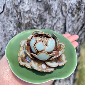 May include: A ceramic lotus flower incense holder. The flower has light blue and brown petals, with a green base. The incense holder is a decorative item, perfect for aromatherapy or meditation.