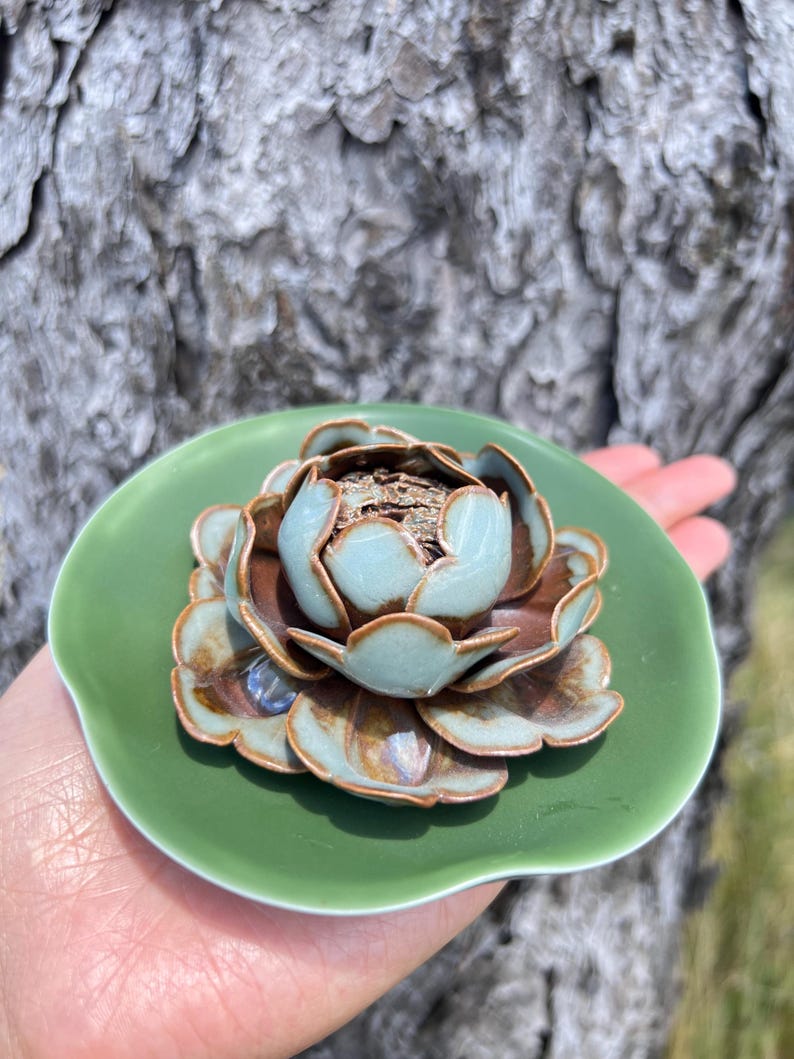 May include: A ceramic lotus flower incense holder. The flower has light blue and brown petals, with a green base. The incense holder is a decorative item, perfect for aromatherapy or meditation.