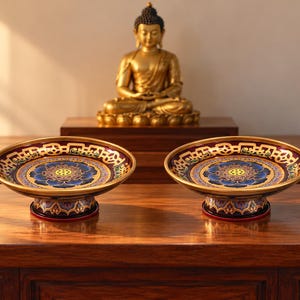 May include: Two matching circular pedestal bowls featuring a deep purple interior with a central blue lotus flower motif, surrounded by intricate gold geometric patterns and a gold rim, supported by a flared base with purple lotus petal designs.