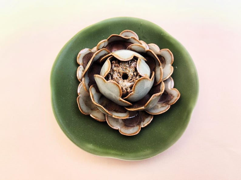 May include: A ceramic decorative piece with a flower design. The flower has layers of brown and light green petals, with a gold-coloured centre. The flower sits on a round, dark green base.