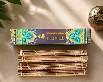May include: A rectangular box of incense sticks featuring a dark purple background with vibrant teal, yellow, and orange decorative patterns and Chinese text. Below the box are four bundles of thin, brown, wooden incense sticks tied with string.