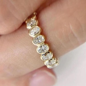 以下が含まれることがあります： ベゼルスタイルでセットされた一連のオーバルカットダイヤモンドを特徴とするゴールドリング。 ダイヤモンドは透明で輝きがあり、リングは研磨仕上げです。 リングはバンドスタイルで、重ね着けや単独での着用に適しています。