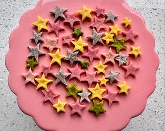 May include: A pink plate with a variety of star-shaped sprinkles in pink, yellow, and green.