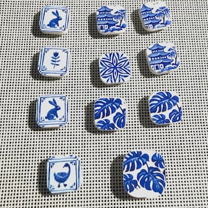 May include: A collection of square, ceramic tiles with blue and white designs. The tiles feature various patterns, including a rabbit, floral motifs, and Asian-inspired landscapes. The tiles are arranged on a white grid.