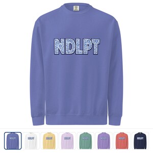 May include: A periwinkle blue sweatshirt with long sleeves. The word "NDLPT" is printed across the chest in a floral design with blue and white accents. Several color options are shown below the sweatshirt.