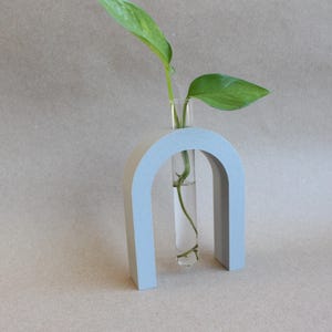 May include: A light blue ceramic arch vase with a clear glass test tube for holding a single stem of greenery.