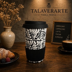 May include: A ceramic travel mug featuring a black and white raised leaf pattern, topped with a black silicone lid and a matching black ribbed silicone grip band around the center. The mug displays a high-contrast design with white organic shapes.