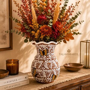 May include: A ceramic vase with a scalloped rim, featuring a brown base with white painted feather-like patterns and butterfly motifs. The vase is filled with a large arrangement of dried flowers in shades of orange, red, and yellow, including eucalyptus.