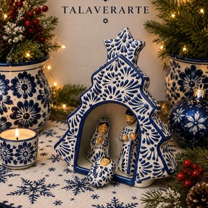 Puede incluir: Un nacimiento de cerámica alojado dentro de una estructura con forma de árbol de Navidad, con patrones florales pintados a mano en azul y blanco. El conjunto incluye figuras de María, José y el niño Jesús, decoradas con diseños azul y blanco.
