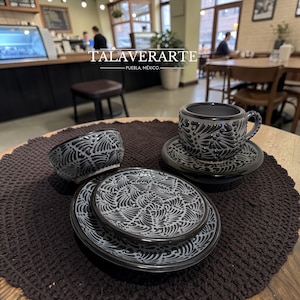 Könnte beinhalten: Ein Set aus Talavera-Keramikgeschirr, darunter eine Tasse mit Untertasse, Schalen und Teller. Die Stücke sind dunkelgrau mit einem weißen Blumenmuster. Der Text "TALAVERARTE - PUEBLA, MÉXICO" ist sichtbar.