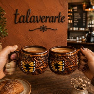 May include: Two round, brown ceramic mugs featuring a raised, textured pattern of monarch butterflies with yellow and black wings. Each mug is filled with a light brown coffee beverage, showcasing a glossy finish and a sturdy, curved handle.