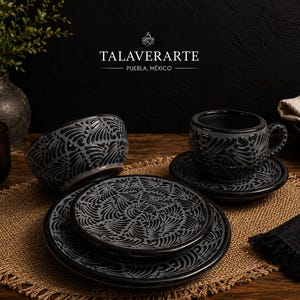 Pode incluir: Um conjunto de louça de cerâmica cinza-escuro com um padrão intrincado de folhas pretas. O conjunto inclui uma tigela, uma xícara com pires e dois pratos empilhados. O texto TALAVERARTE PUEBLA, MÉXICO é visível na parte superior central.