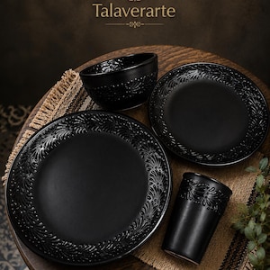 Puede incluir: Un juego de vajilla de cerámica negro mate que incluye un plato grande, un plato pequeño, un cuenco y un vaso. Cada pieza presenta un patrón floral en relieve detallado a lo largo del borde. El texto Talaverarte es visible en la imagen.