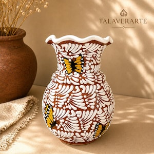 May include: A ceramic vase with a brown base colour, featuring a white scalloped rim and intricate white painted patterns covering the surface. Three yellow and black butterfly motifs are painted on the exterior. The text TALAVERARTE is visible.